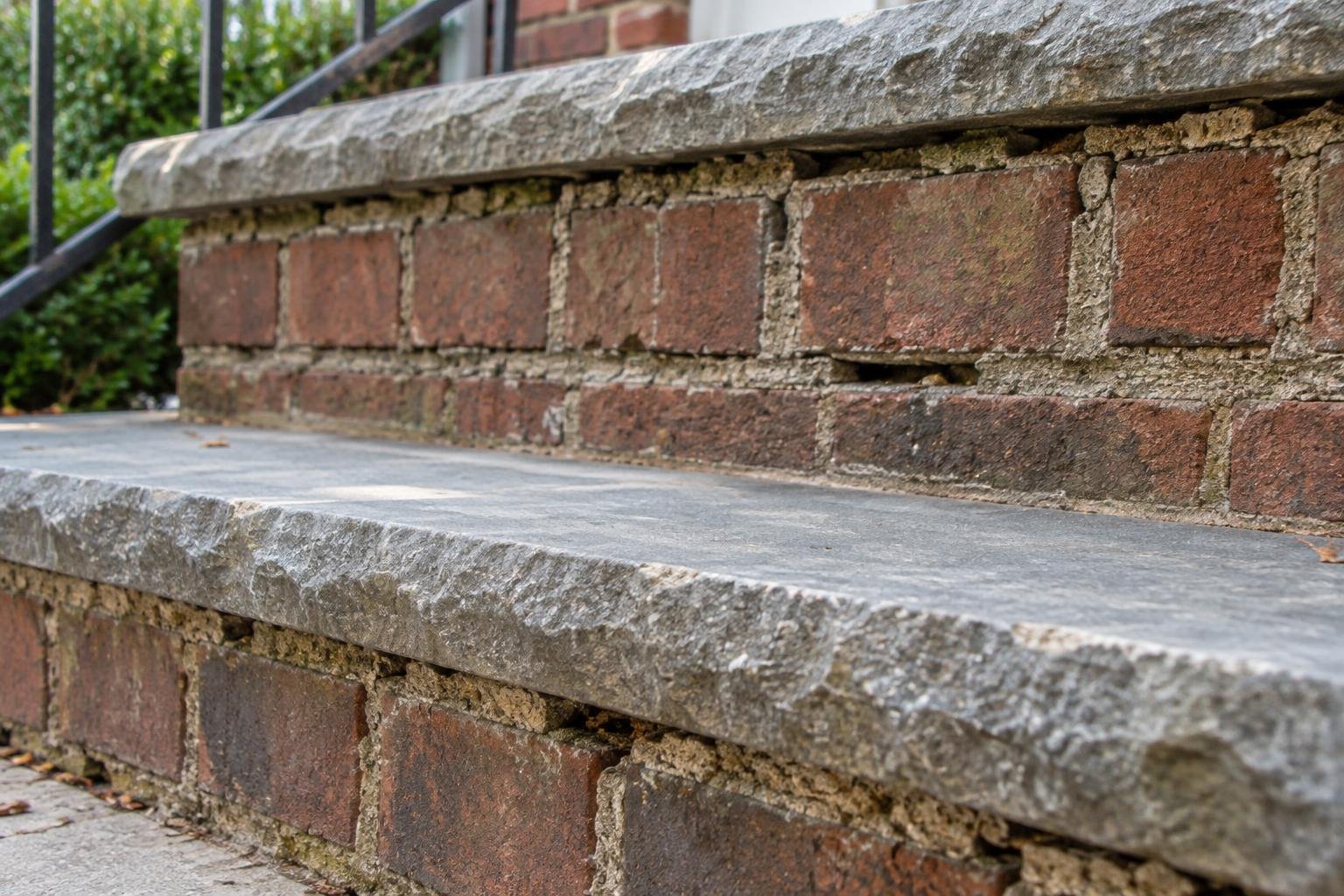 Open mortar joints beneath a stone tread on brick entrance steps.