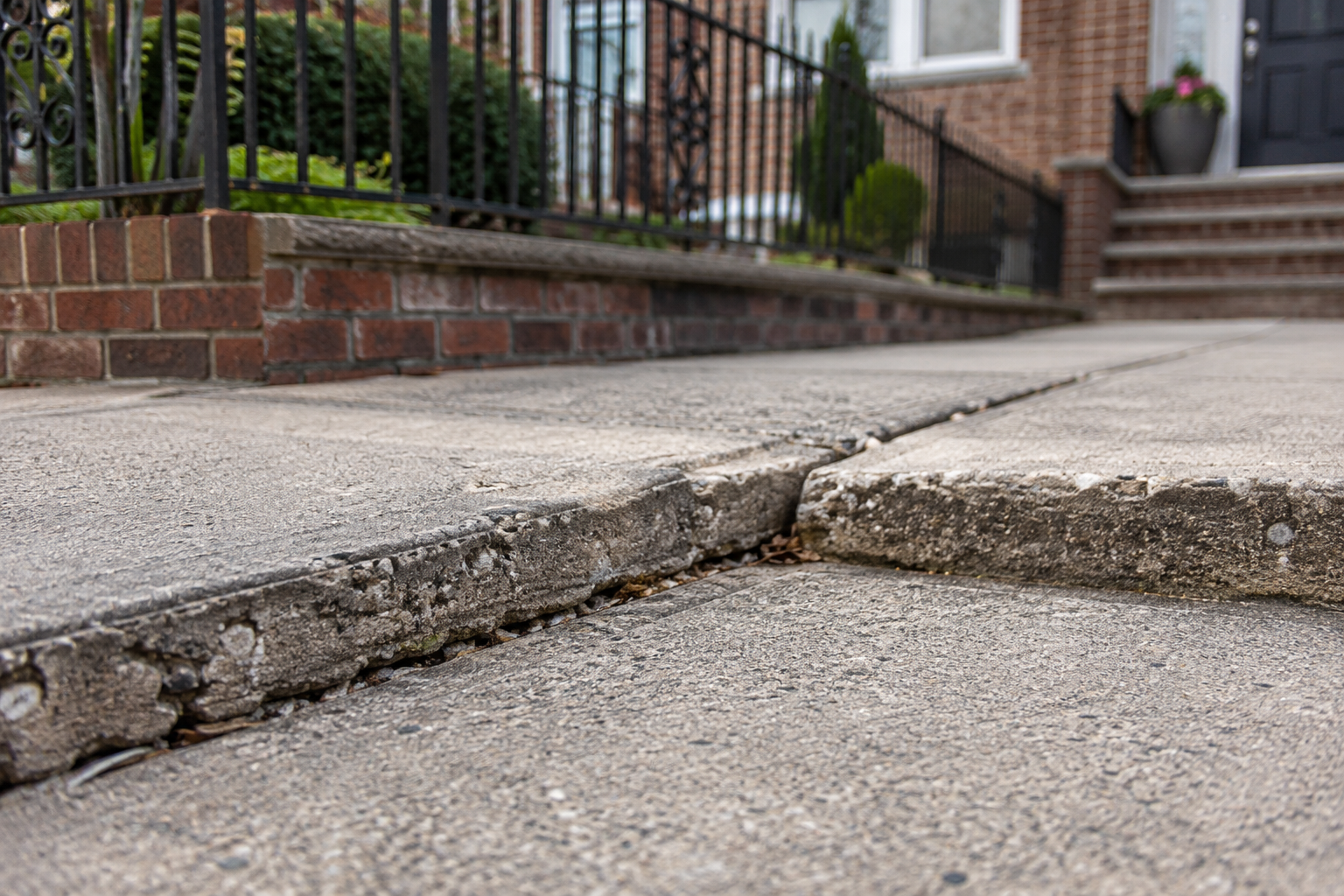 Raised edge between concrete walkway slabs showing a trip hazard and localized surface wear.